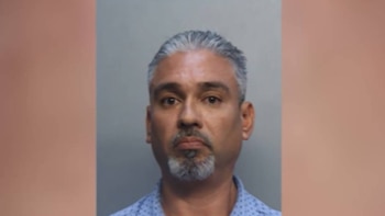 Retrato de un hombre de mediana edad con cabello canoso y barba de chivo, mirando directamente a la cámara sobre un fondo gris claro. Viste camisa azul