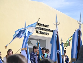 Varios estudiantes sostienen banderas argentinas y bonaerenses frente al cartel de la Escuela de Educación Secundaria Técnica Número 1