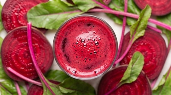 Vaso de jugo de remolacha con burbujas, rodajas gruesas de remolacha y hojas verdes alrededor.