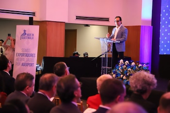 Un hombre con gafas habla tras un atril transparente junto a un cartel de Made in Guatemala frente a un público sentado