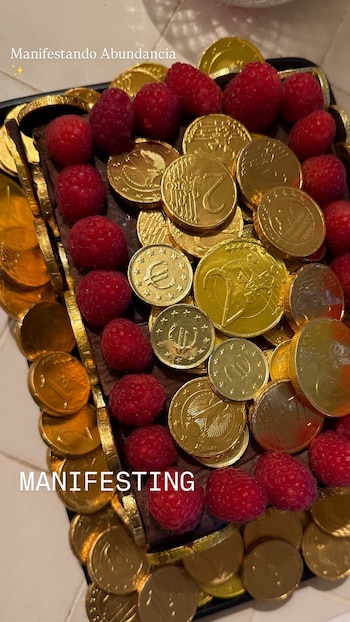 Primer plano de un postre rectangular oscuro decorado con numerosas monedas de chocolate dorado que simulan euros y frambuesas rojas frescas, dispuestas alternadamente sobre la superficie