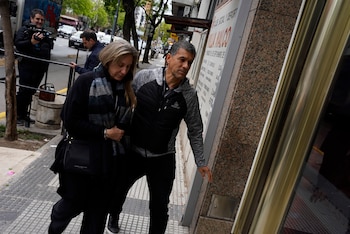 Un hombre y una mujer caminan por una acera hacia una puerta mientras una persona con una cámara los graba desde la calle