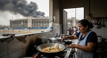 Mujer cocina chaufa en una cocina humilde, con humo negro que se eleva sobre el Estadio Monumental de fondo visto a través de una puerta abierta