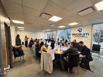Vista de una sala de reuniones con personas sentadas alrededor de una mesa, una mujer presentando frente a una pantalla proyectada y el logo de aecaum en la pared