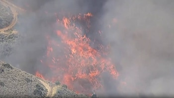 Imagen aérea de un gran incendio forestal con llamas rojas brillantes y humo gris que consume la vegetación seca en una ladera
