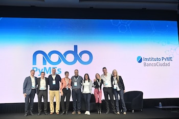 Nueve personas alineadas en un escenario sonríen ante una pantalla con logotipos de Nodo PyMEs y Banco Ciudad