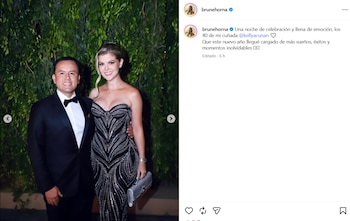 Un hombre con esmoquin negro y una mujer con un vestido de noche posan frente a un fondo de follaje verde