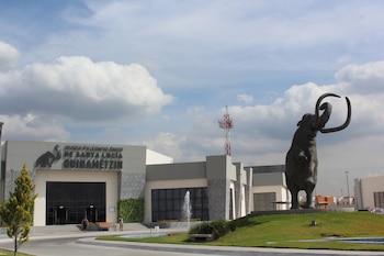 Exterior del Museo Paleontológico de Santa Lucía Quinametzin con una gran estatua de mamut, césped, una fuente y un cielo nublado