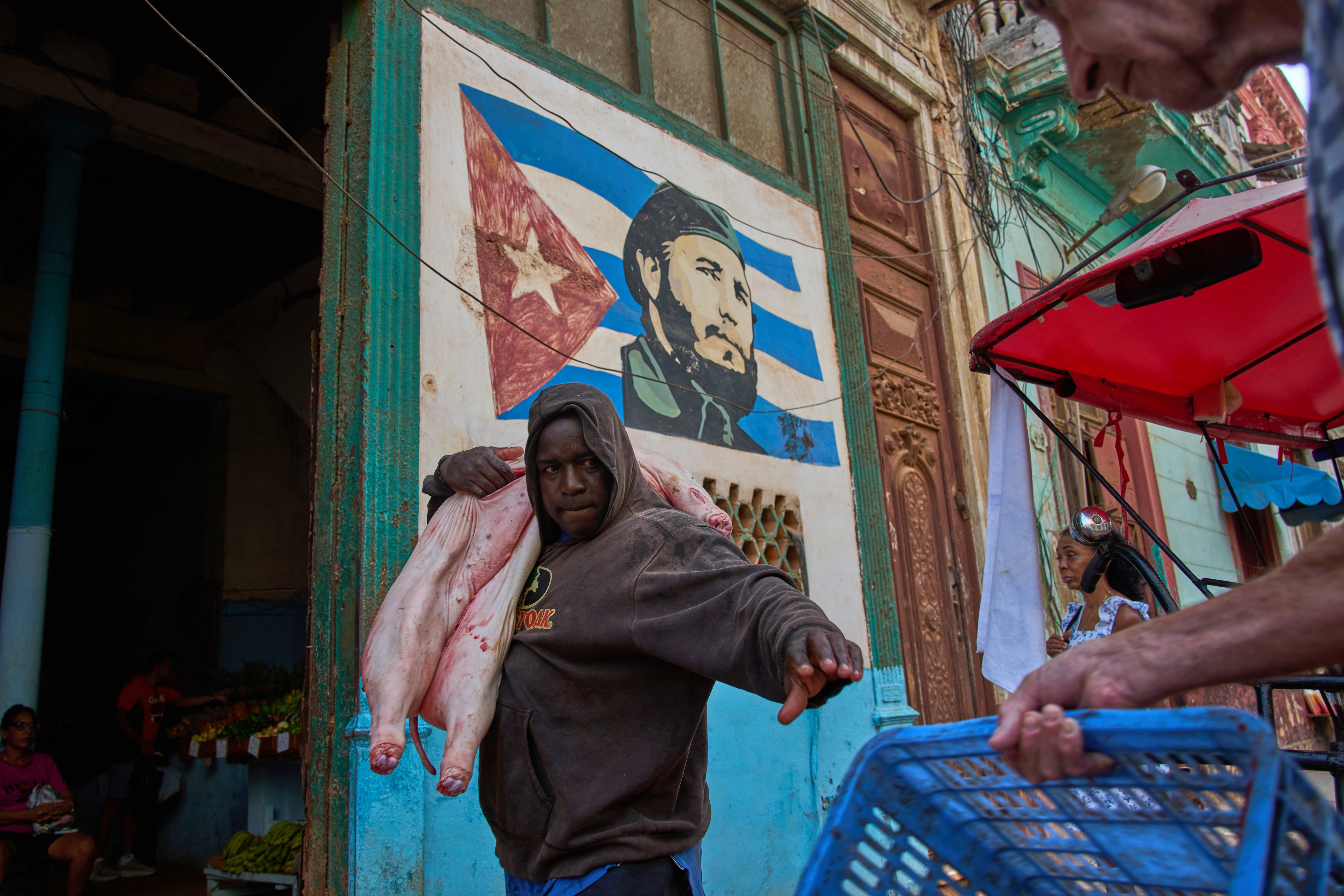 Un hombre carga un cerdo a la entrada de un mercado decorado con un mural de Fidel Castro, el miércoles 12 de agosto de 2026, en La Habana, Cuba (AP Foto/Ramón Espinosa)