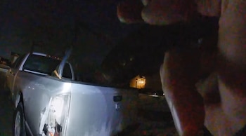 Vista nocturna de la parte trasera de una camioneta plateada con el faro trasero izquierdo dañado o faltante. Se aprecian partes del vehículo rotas