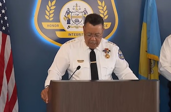 Un hombre uniformado habla desde un podio de madera frente a un emblema policial y las banderas de Estados Unidos y de Filadelfia