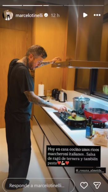 Hombre con tatuajes en ambos brazos, vestido de negro, cocina en una estufa de inducción. Agita el contenido de una sartén con una cuchara de madera en una cocina moderna