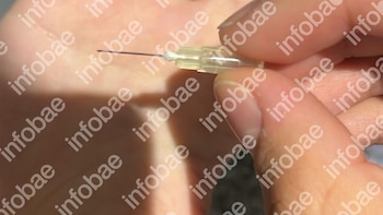 Primer plano de una mano sosteniendo una aguja hipodérmica. Se distingue la aguja metálica y su conector de plástico transparente