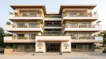 Fachada de un edificio moderno de tres niveles con balcones, plantas, rampas de acceso y dos emblemas en forma de árbol junto a la entrada.