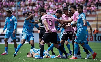 Varios futbolistas con camisetas rosadas y celestes discuten frente al árbitro mientras un jugador permanece tendido en el césped