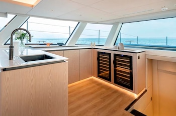 Cocina de una embarcación con encimera blanca, fregadero, refrigeradores para botellas y ventanales con vista al mar