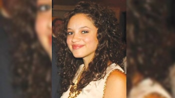 Fotografía en plano medio corto de una mujer con cabello largo rizado y blusa clara con detalles dorados