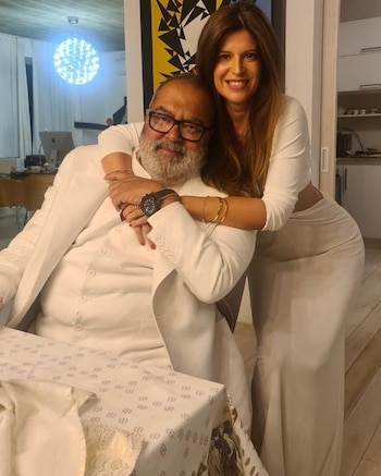 Elba Marcovecchio, con cabello castaño y sonrisa, abraza por detrás a Jorge Lanata, quien está sentado, con barba, gafas y vestido de blanco