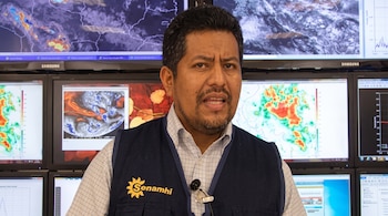 Hombre con chaleco azul del Senamhi frente a varios monitores que muestran mapas del tiempo y radares meteorológicos.