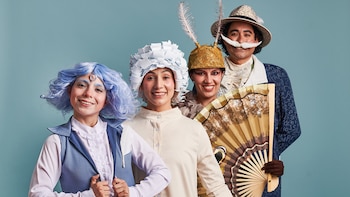 Cuatro personas disfrazadas con vestuario teatral sonríen. Hay una mujer con peluca azul, dos mujeres con tocados y un hombre con sombrero y bigote falso