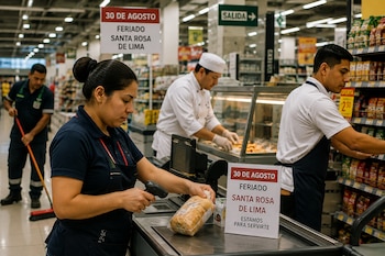 Una cajera escanea un producto en la caja de un supermercado con carteles informativos sobre el feriado del 30 de agosto