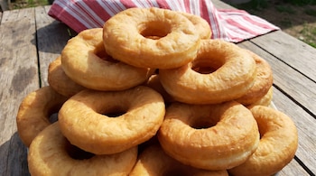 Montón de tortas fritas argentinas de color dorado sobre una mesa de madera, con un paño rayado rojo y blanco de fondo.