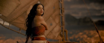 Joven con cabello oscuro y top rojo estampado en una canoa con vela, mirando hacia arriba con expresión de asombro. El cielo oscuro y el mar brillante son visibles al fondo