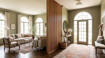 Sala de estar con sofás y ventanales separada del recibidor y la puerta principal por una pared de listones verticales de madera.