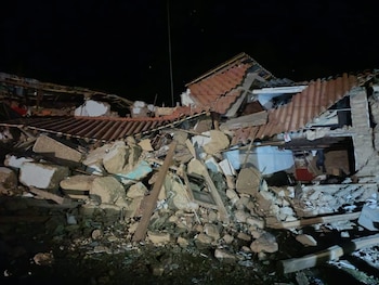 Restos de un edificio derrumbado de noche, con techos de tejas rotos y un gran cúmulo de escombros