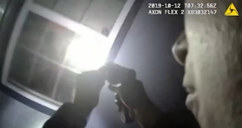 Captura de cámara corporal en la que un agente sostiene una linterna y un arma de fuego frente a una ventana en la oscuridad
