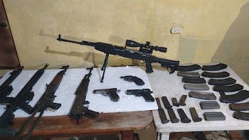 Varias armas de fuego sobre dos mesas: un rifle de francotirador con mira, cuatro rifles semiautomáticos, dos pistolas, un revólver y muchos cargadores