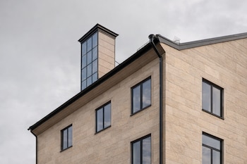 Fachada de edificio de bloques claros con ventanas de marco oscuro, tejado inclinado con canalones y una chimenea acristalada en la parte superior.