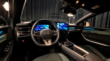 El interior de un vehículo con volante con el logo de Renault, pantallas digitales encendidas y luces ambientales en el tablero