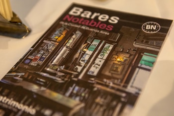 Portada de libro titulada 'Bares Notables de la Ciudad de Buenos Aires' con una ilustración de un bar. Se observan logos de tarjetas y la palabra 'Patrimonio'