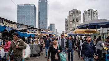 Peatones caminan junto a carritos de comida y puestos callejeros, con modernos edificios y rascacielos en el fondo.