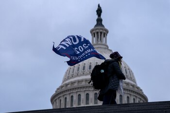 A demonstrator carries a "Trump 2020" flag outside the U.S. Capitol in Washington, D.C., U.S., on Wednesday, Jan. 6, 2021. The House and Senate will meet in a joint session today to count the Electoral College votes to confirm President-elect Joe Biden's victory, but not before a sizable group of Republican lawmakers object to the counting of several states' electors.