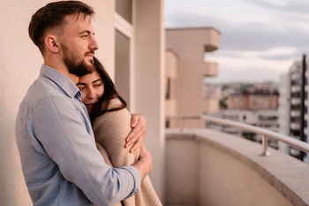Un chico y una chica abrazados en un balcón mirando el horizonte
