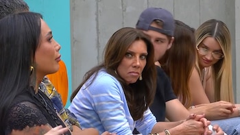 Cynthia Klitbo con blusa azul a rayas y collar dorado, sentada junto a tres personas. Una mujer con blusa negra y tatuajes, y otra con gafas