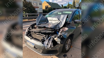 Un automóvil gris con el capó totalmente deformado, el parabrisas trizado y la parte delantera destruida junto a la acera.