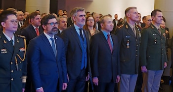 Un grupo de hombres con trajes formales y uniformes militares permanecen de pie alineados en un salón