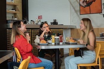 Tres amigas comen hamburguesas mientras charlan (Pexels)