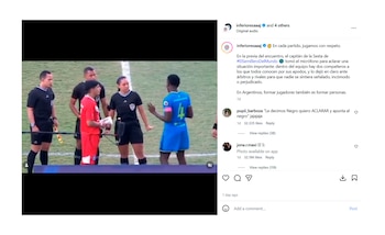 Cinco personas en un campo de fútbol: tres árbitros (dos hombres, una mujer), un jugador con camiseta roja y otro con camiseta azul número 4. El jugador de rojo sostiene un objeto blanco