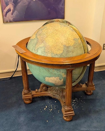 Un gran globo terráqueo sobre una base de madera tallada con pequeños fragmentos claros esparcidos sobre la alfombra azul