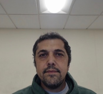 Primer plano de un hombre de mediana edad con cabello oscuro y barba, usando una chaqueta verde, mirando al frente