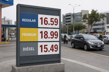 Panel gris de una estación con precios de combustible regular, premium y diésel, junto a una avenida con automóviles.