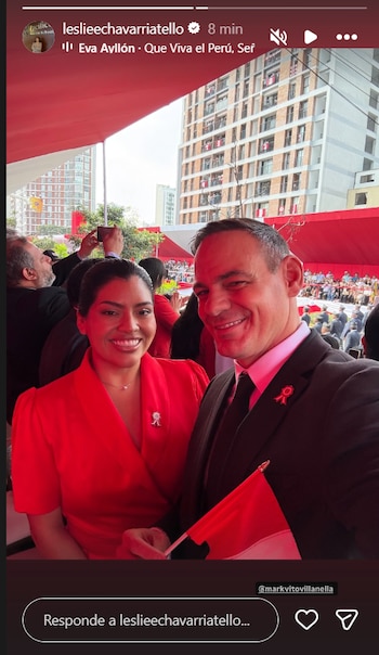 Un hombre y una mujer sonríen a cámara. El hombre viste traje oscuro y sostiene una bandera de Perú. La mujer lleva un vestido rojo. Ambos portan un pin