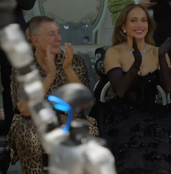 Jennifer Lopez luce un vestido negro y guantes largos mientras aplaude junto a Stefano Gabbana y un dispositivo robótico en primer plano