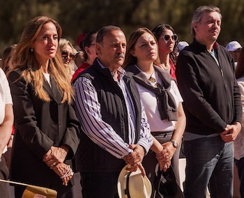 Cuatro personas en primer plano: mujer de blazer negro, hombre de chaleco y camisa a rayas, mujer con suéter al hombro, y hombre de chaqueta negra. Varias personas en segundo plano borroso