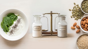 Composición de alimentos saludables y suplementos: yogur, espinacas, chía, semillas de calabaza, almendras, arroz integral. Frascos de calcio, magnesio y balanza.