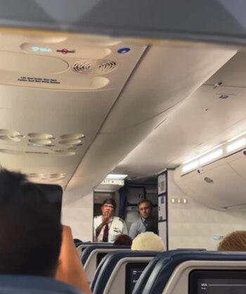 Interior de la cabina de un avión Delta, mostrando un piloto y otro miembro de la tripulación en el pasillo, con asientos de pasajeros en primer plano